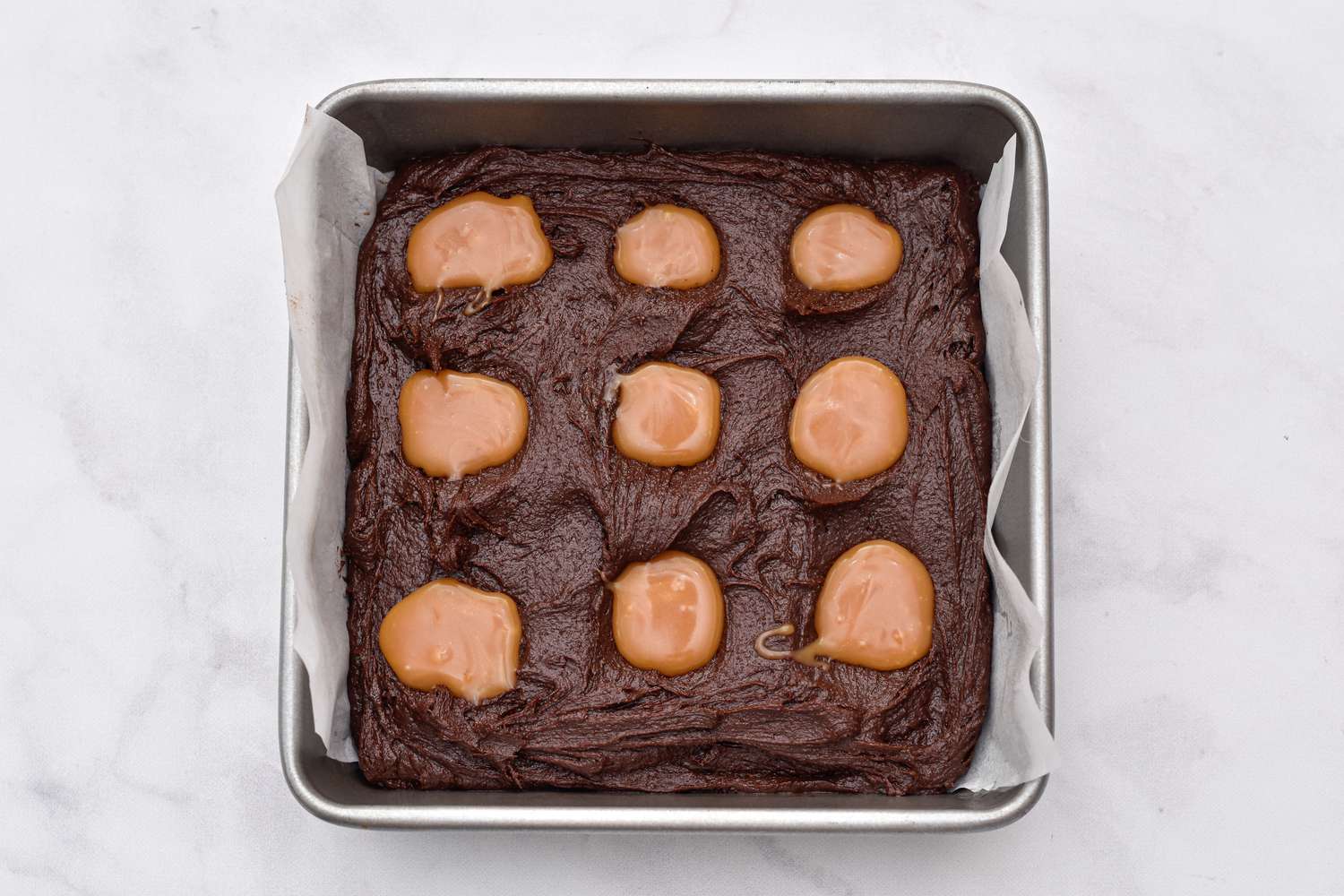 Caramel dolloped on brownie batter for Caramel Swirl Brownies