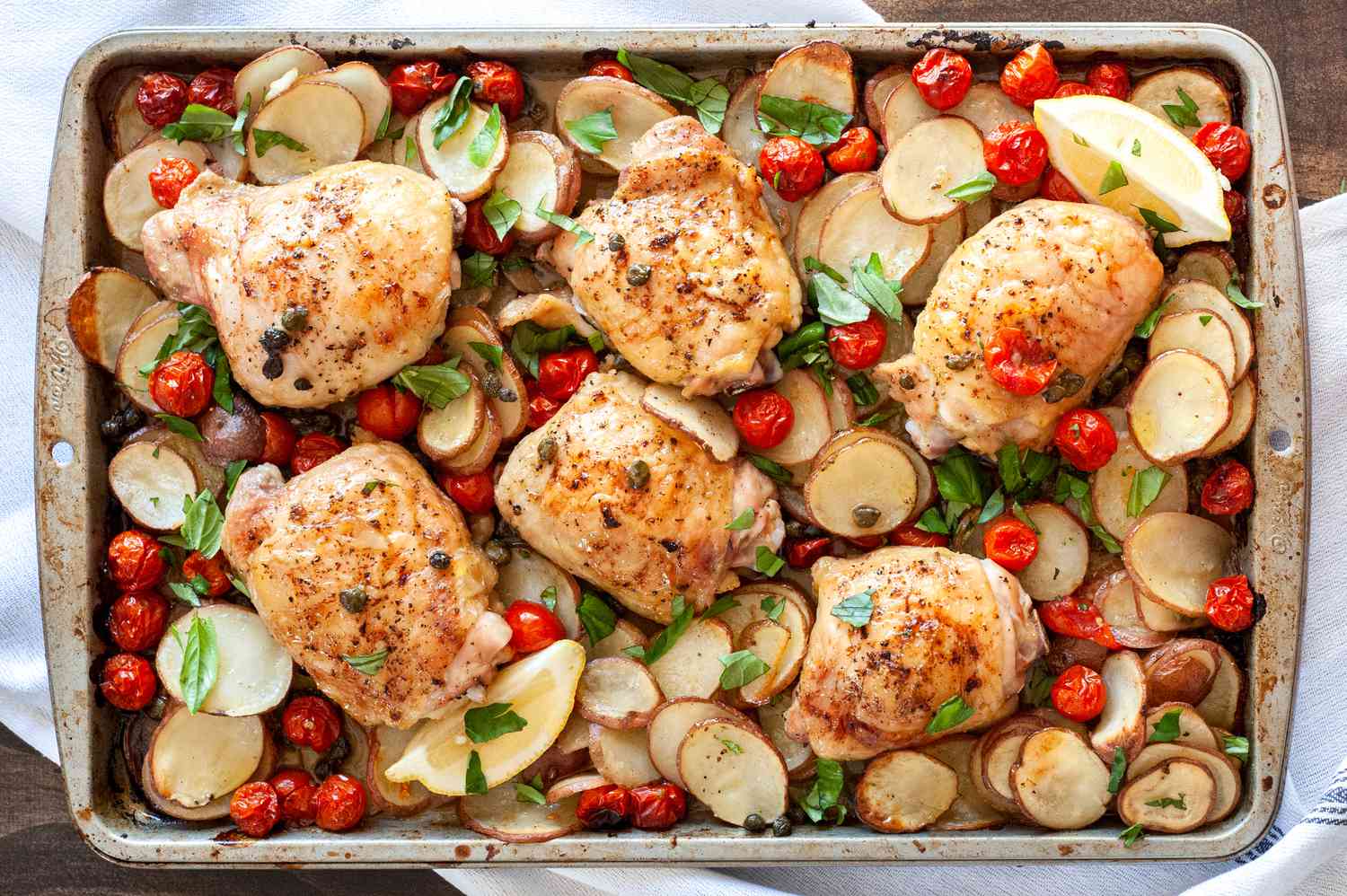 Vue de haut de cuisses de poulet sur plaque avec tomates, pommes de terre, câpres et basilic sur une plaque