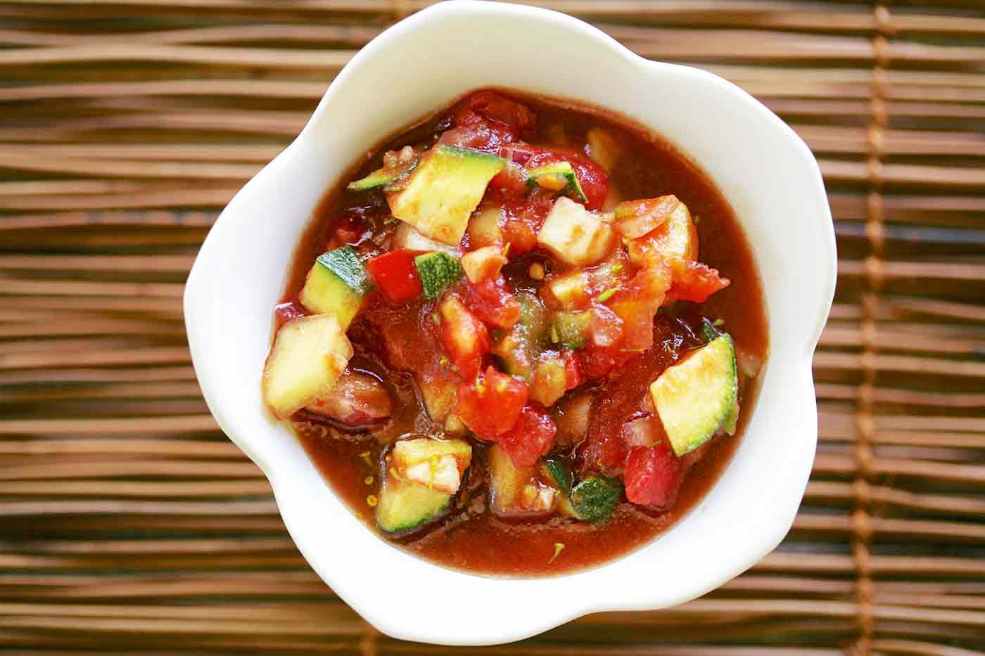 Un bol de soupe froide de légumes d'été aux tomates sur un set de table.