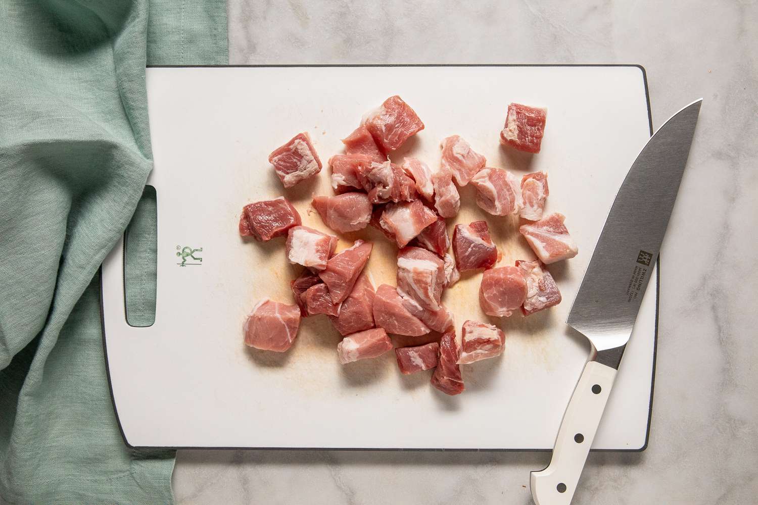 porc découpé en cubes sur une planche à découper avec un couteau