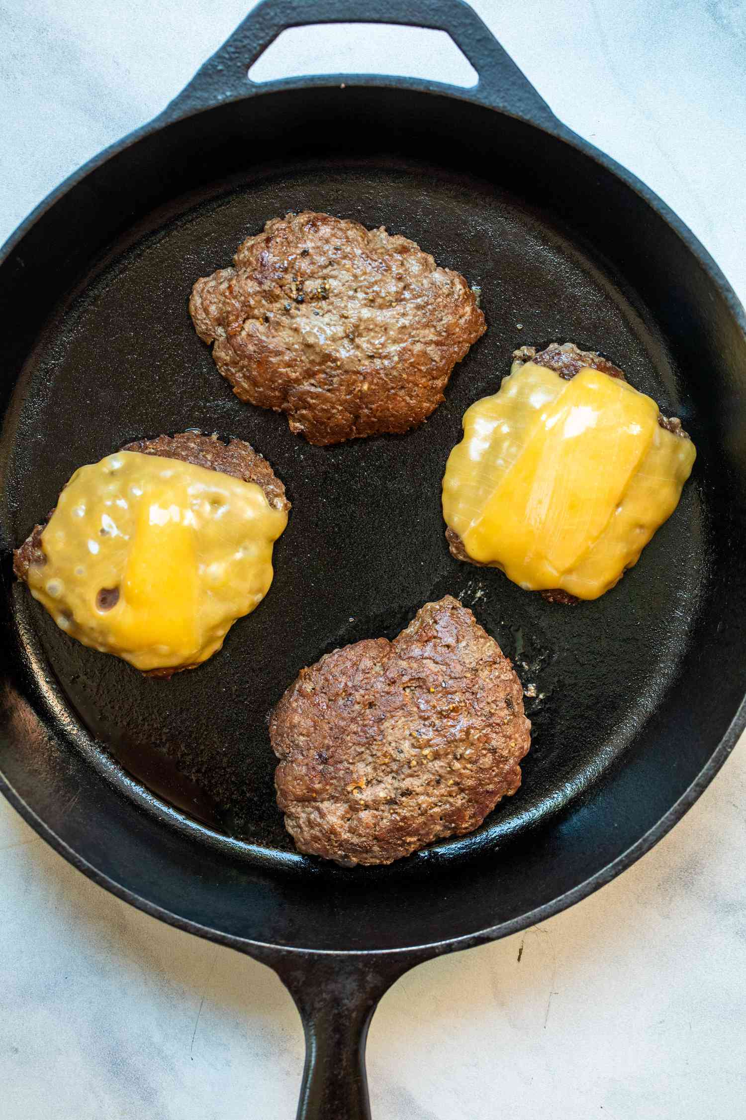 Quatre hamburgers dans une poêle en fonte avec deux galettes couvertes de fromage fondu