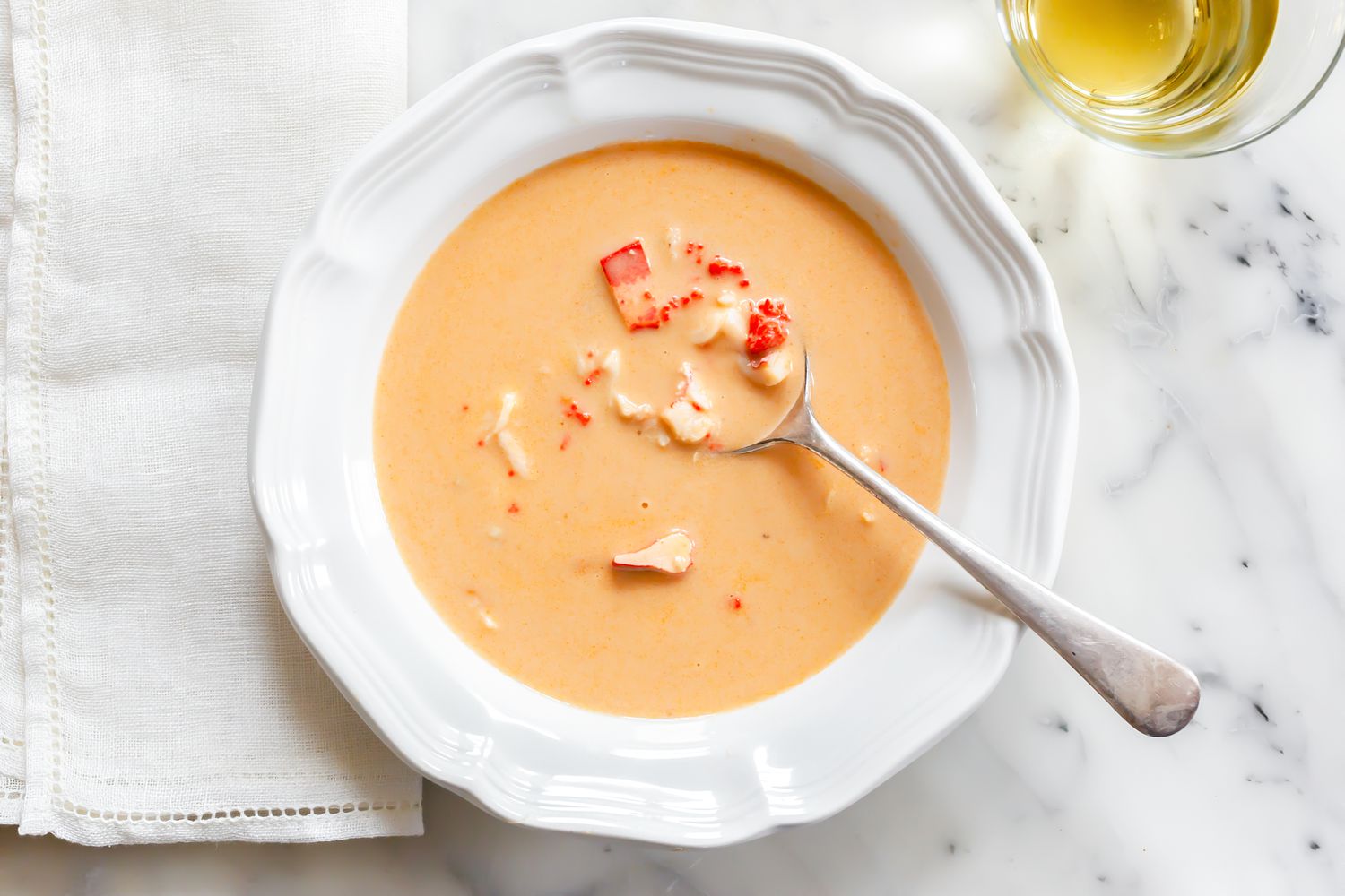 Bol de bisque de homard avec une cuillère à côté d'une serviette et d'un verre