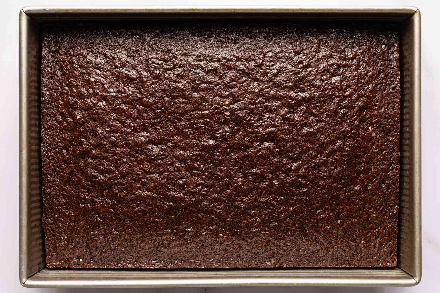 Vue de dessus de l'appareil cuit dans un plat à pâtisserie rectangulaire en métal pour la recette de gâteau Brooklyn Blackout facile