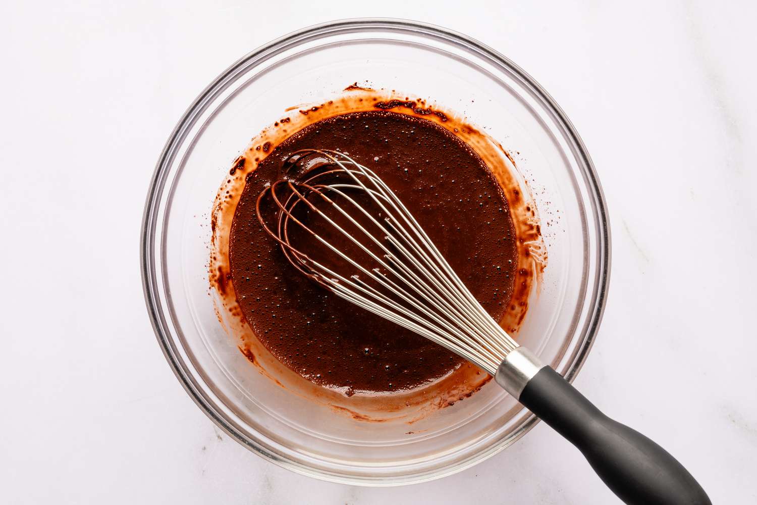 Vue de dessus d'un bol en verre transparent et d'un fouet avec du cacao et de l'eau chaude après mélange pour la recette de gâteau Brooklyn Blackout facile