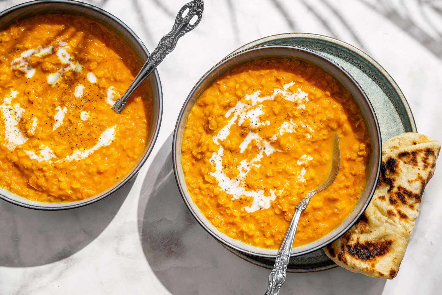 Soupe de lentilles à la noix de coco dans deux bols avec des cuillères, garnie de sauce au yaourt, naan sur le côté