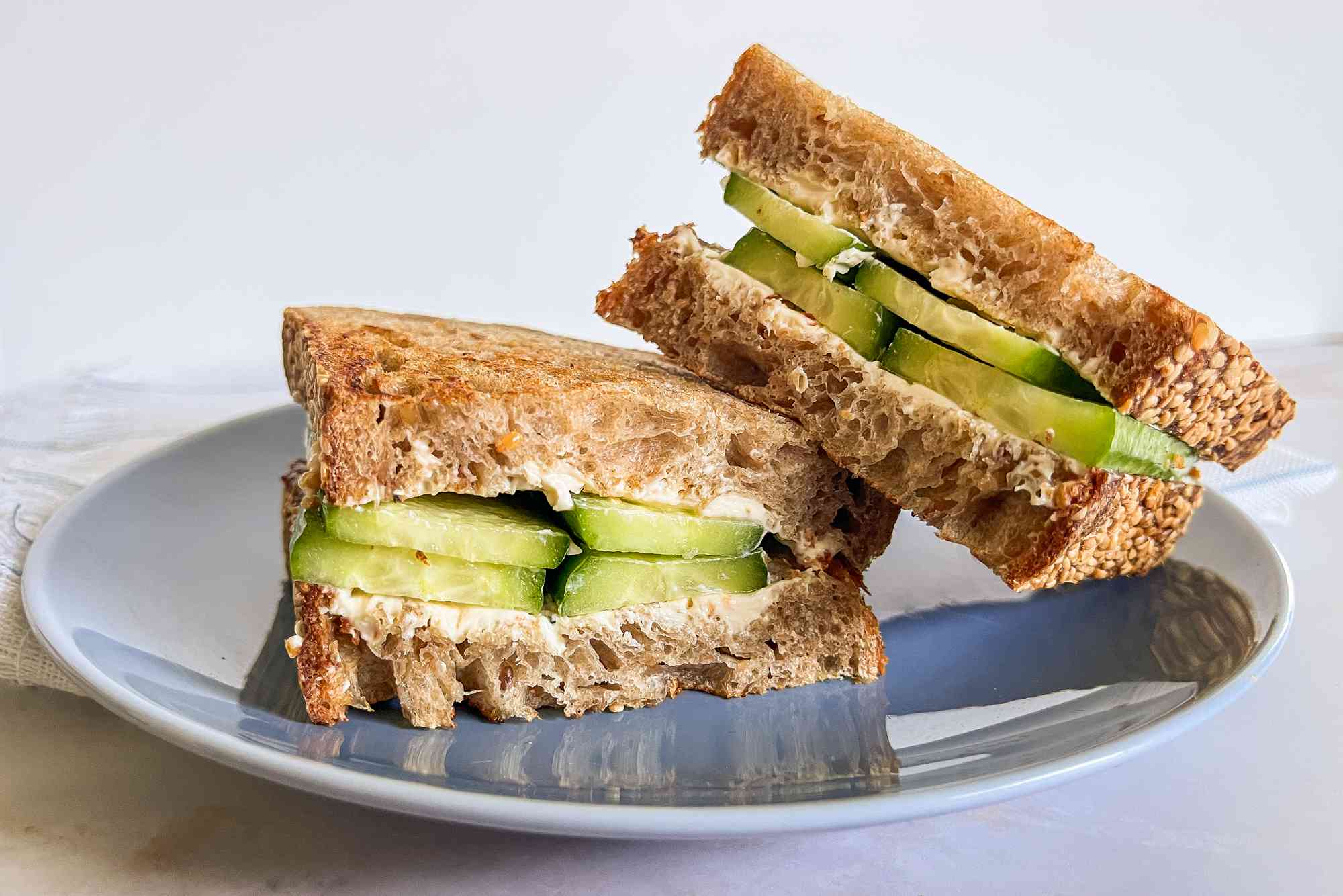 Halved 2-ingredient cucumber sandwich on a plate, with one sandwich half leaned on another 