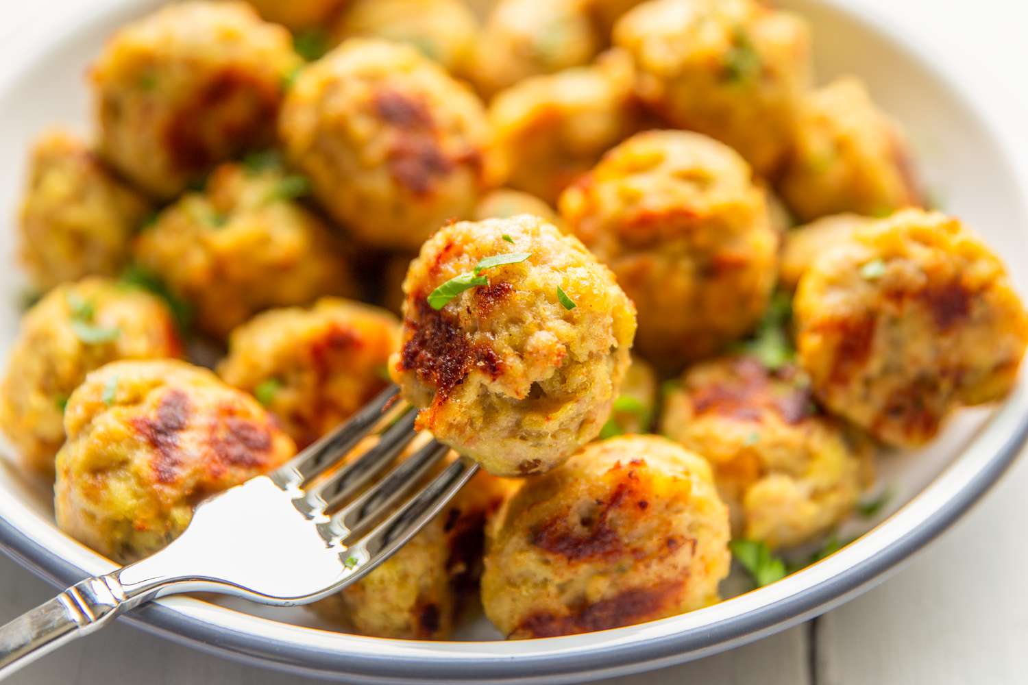 Gros plan d'une fourchette tenant une boulette de poulet à 3 ingrédients devant un bol de boulettes.