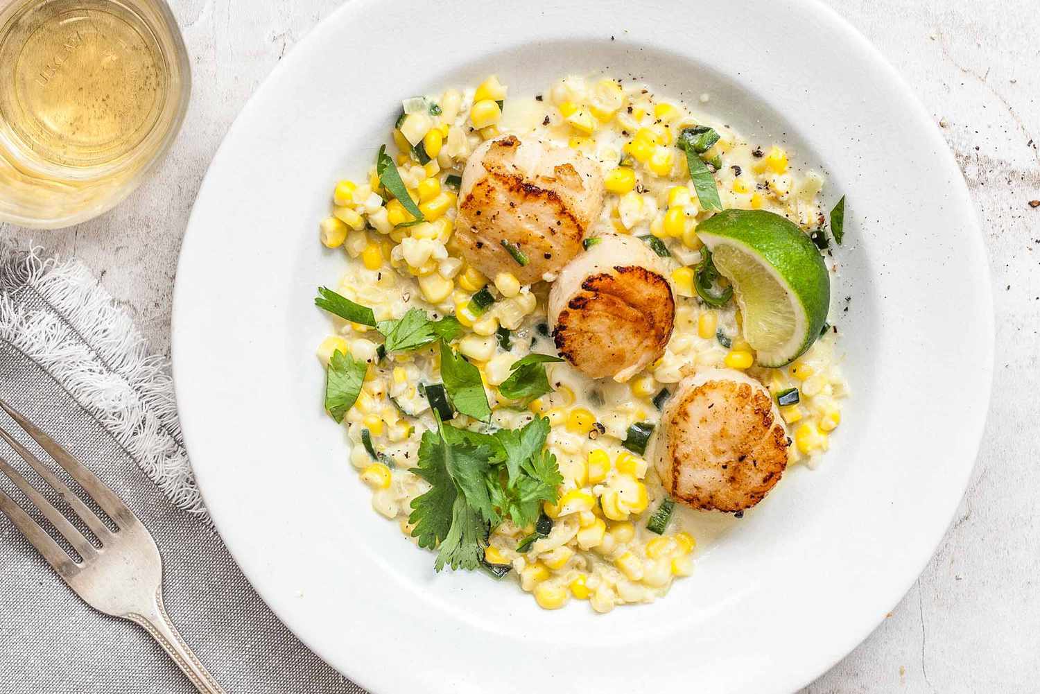 scallops poêlés avec du maïs crémeux et de la lime sur une assiette blanche