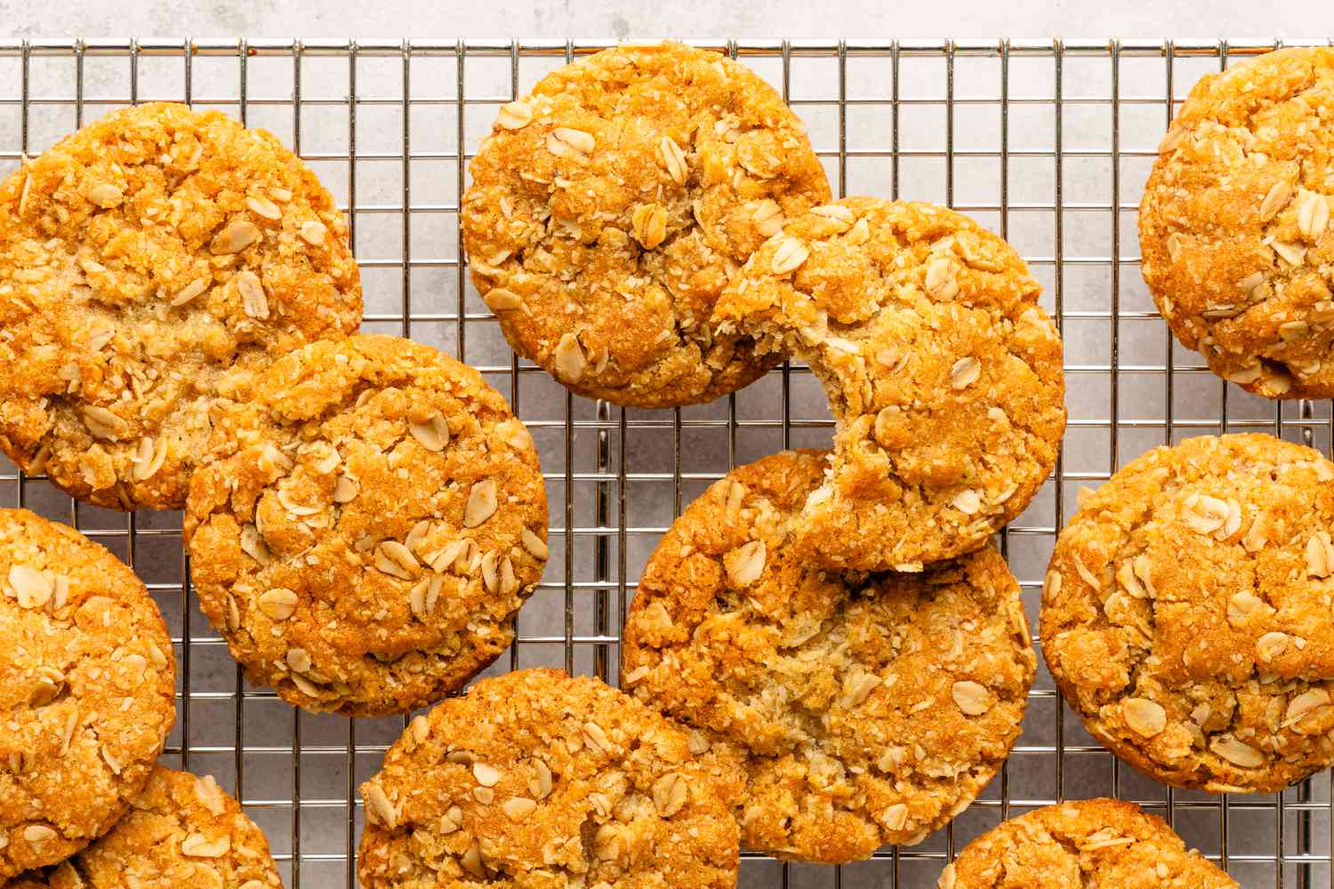 biscuits Anzac sur une grille de refroidissement, avec une bouchée prise dans l'un des biscuits