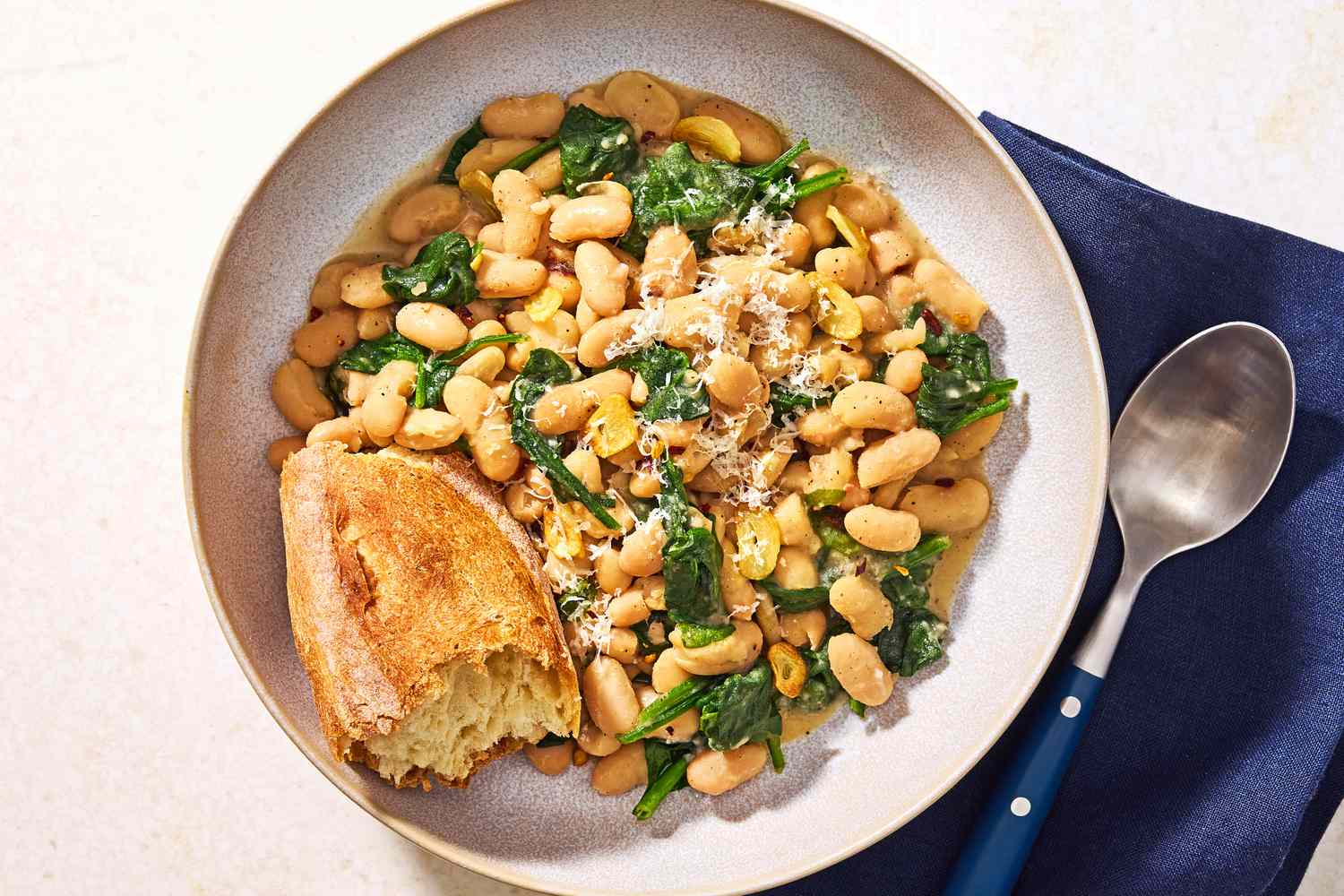 Vue aérienne d'un bol de Haricots et Légumes en 10 Minutes avec un bout de pain à côté d'une cuillère et reposant sur une serviette bleue