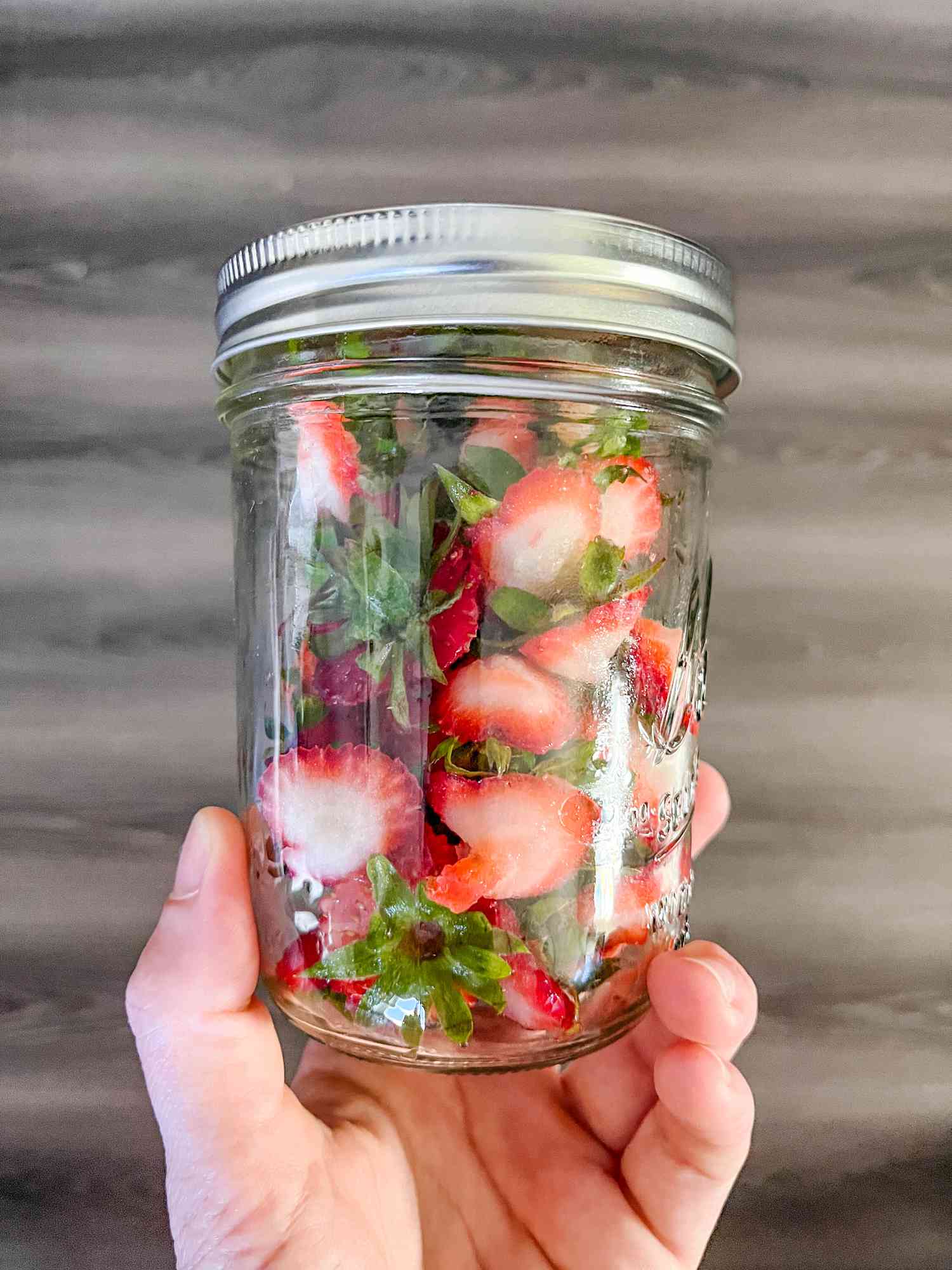 Jar of Strawberry Tops Held by Hand