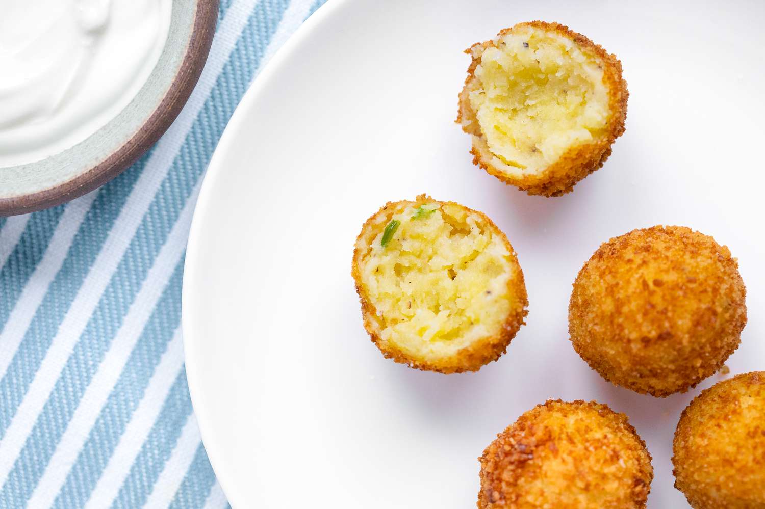 Croquettes de pommes de terre sur une assiette avec l'une d'elles cassée en deux, et à côté de l'assiette, une petite soucoupe avec de la sauce