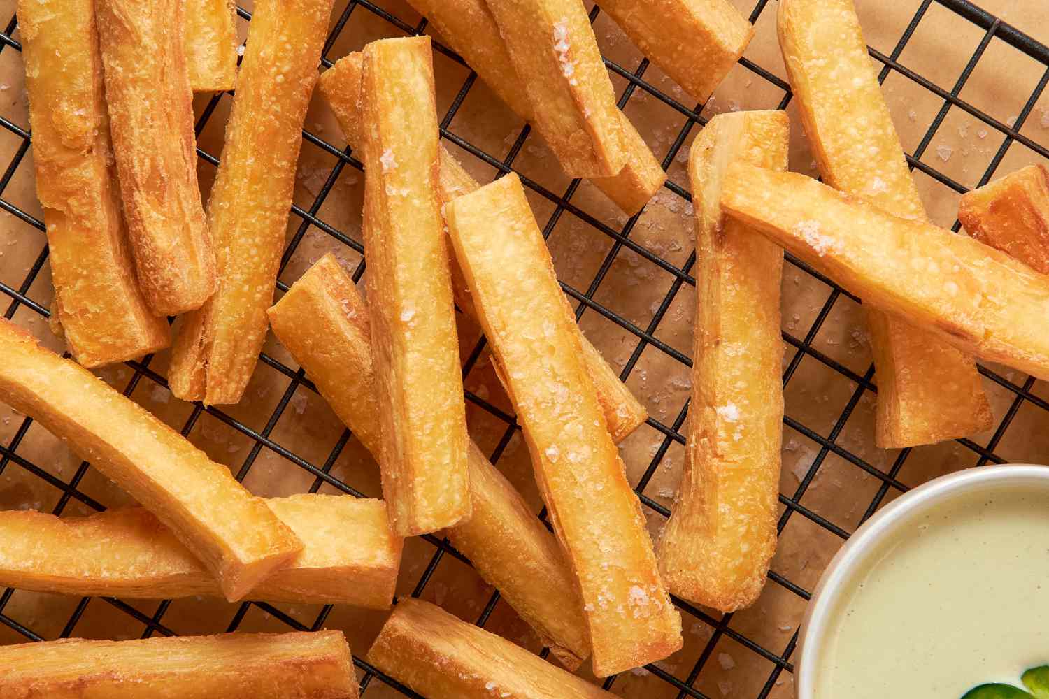 Yuca Fries on a Cooling Rack With a Bowl of Spicy Mayo, and Underneath the Cooling Rack, Parchment Paper