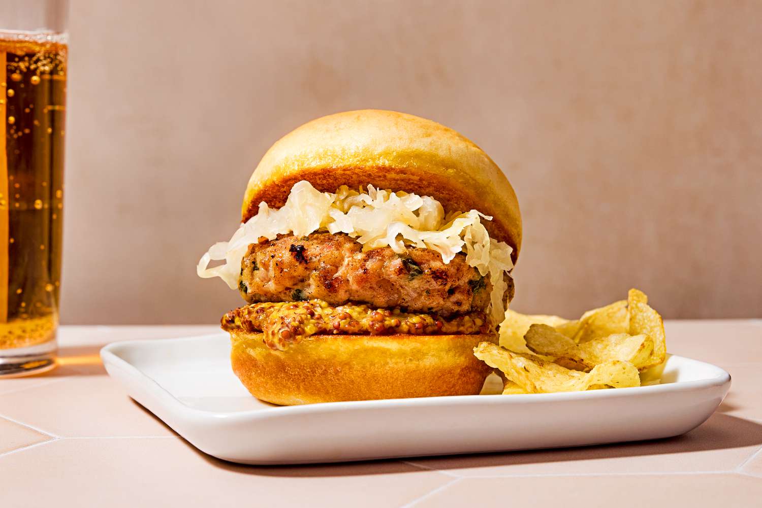 Vue de côté d'un slider de bratwurst garni de choucroute, sur une assiette avec des chips de pomme de terre et un verre de bière en arrière-plan