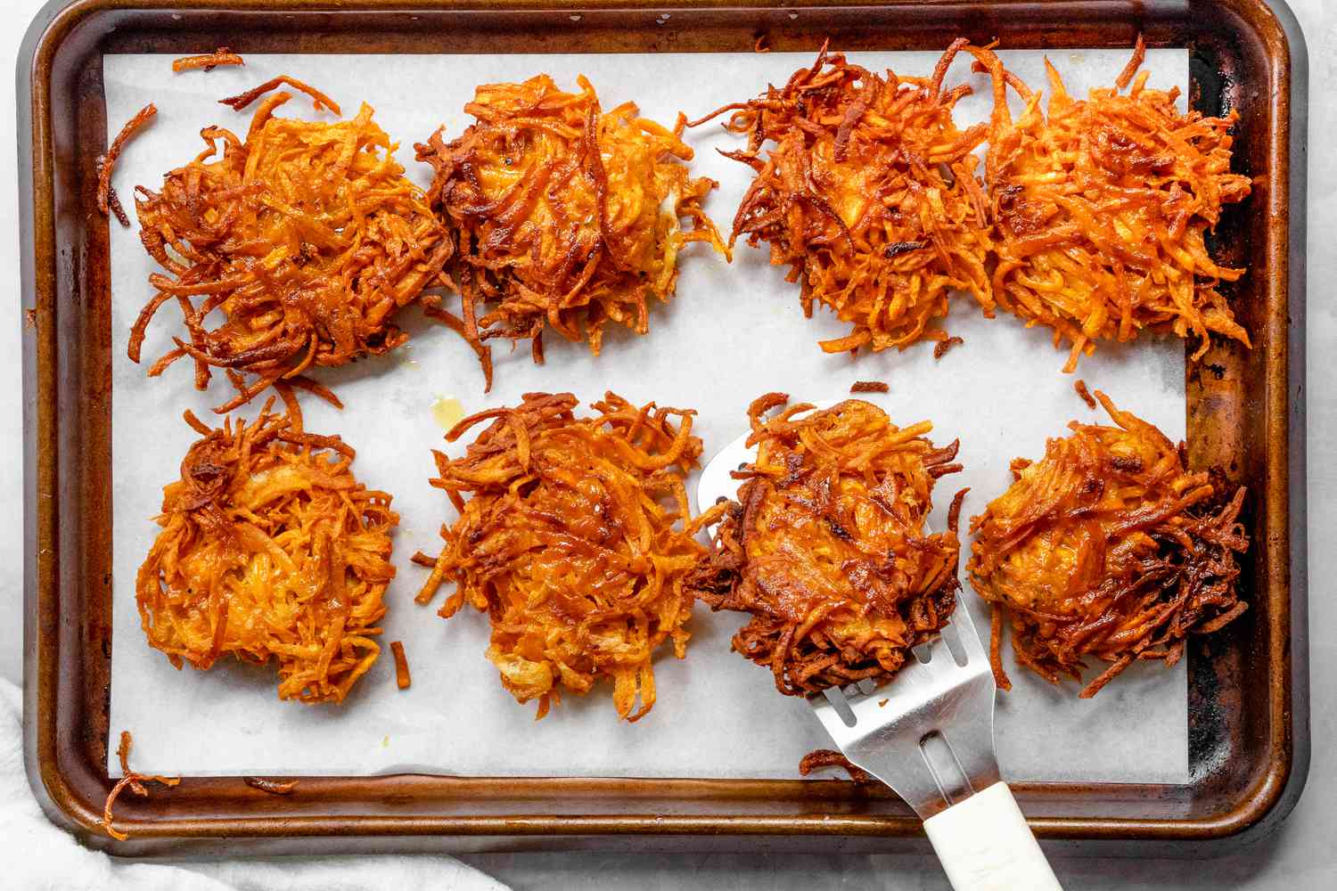 Latkes de patate douce sur une plaque de cuisson recouverte de papier sulfurisé avec une sur une spatule