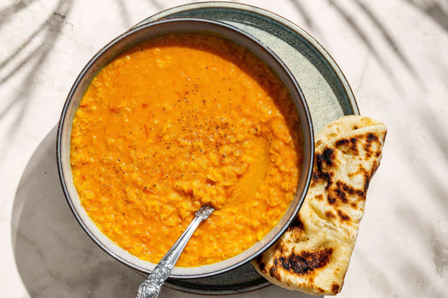 Soupe de lentilles à la noix de coco dans un bol avec du naan sur le côté