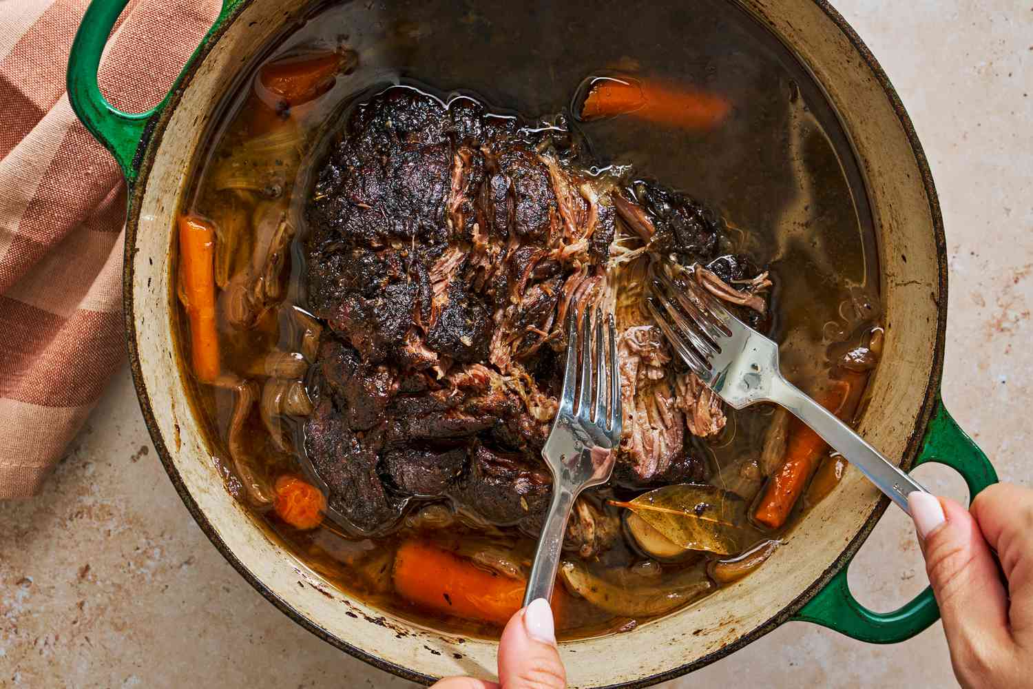 Une cocotte de pot-au-feu et des mains tenant deux grandes fourchettes, effilochant la viande