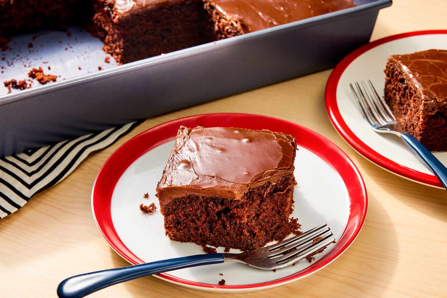 Deux petites assiettes de gâteau Coca-Cola avec des fourchettes devant un moule à gâteau en métal sur une table en bois