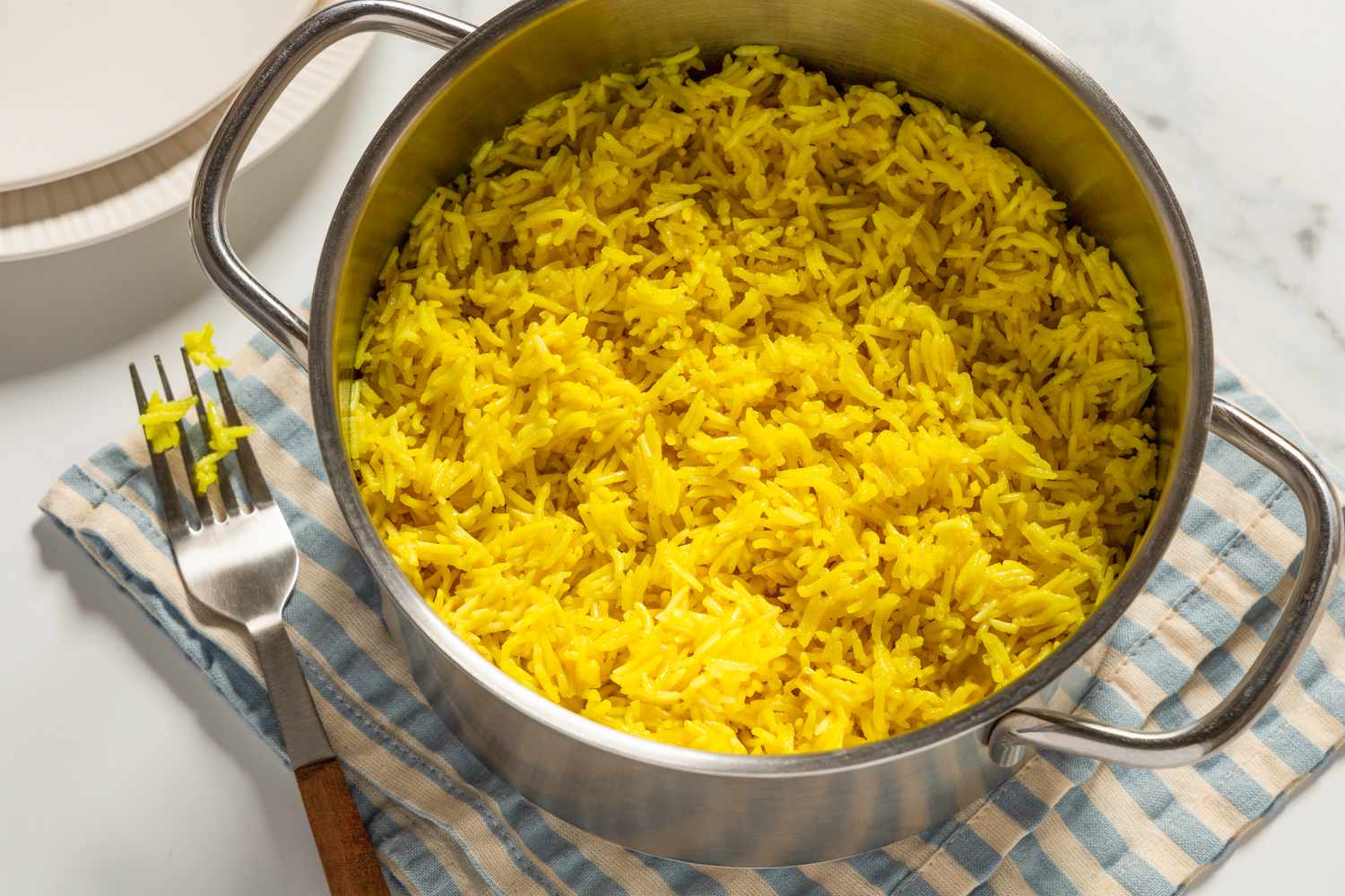 Vue de dessus d'une casserole de riz doré sur un comptoir en marbre avec une serviette en tissu, une fourchette et des assiettes