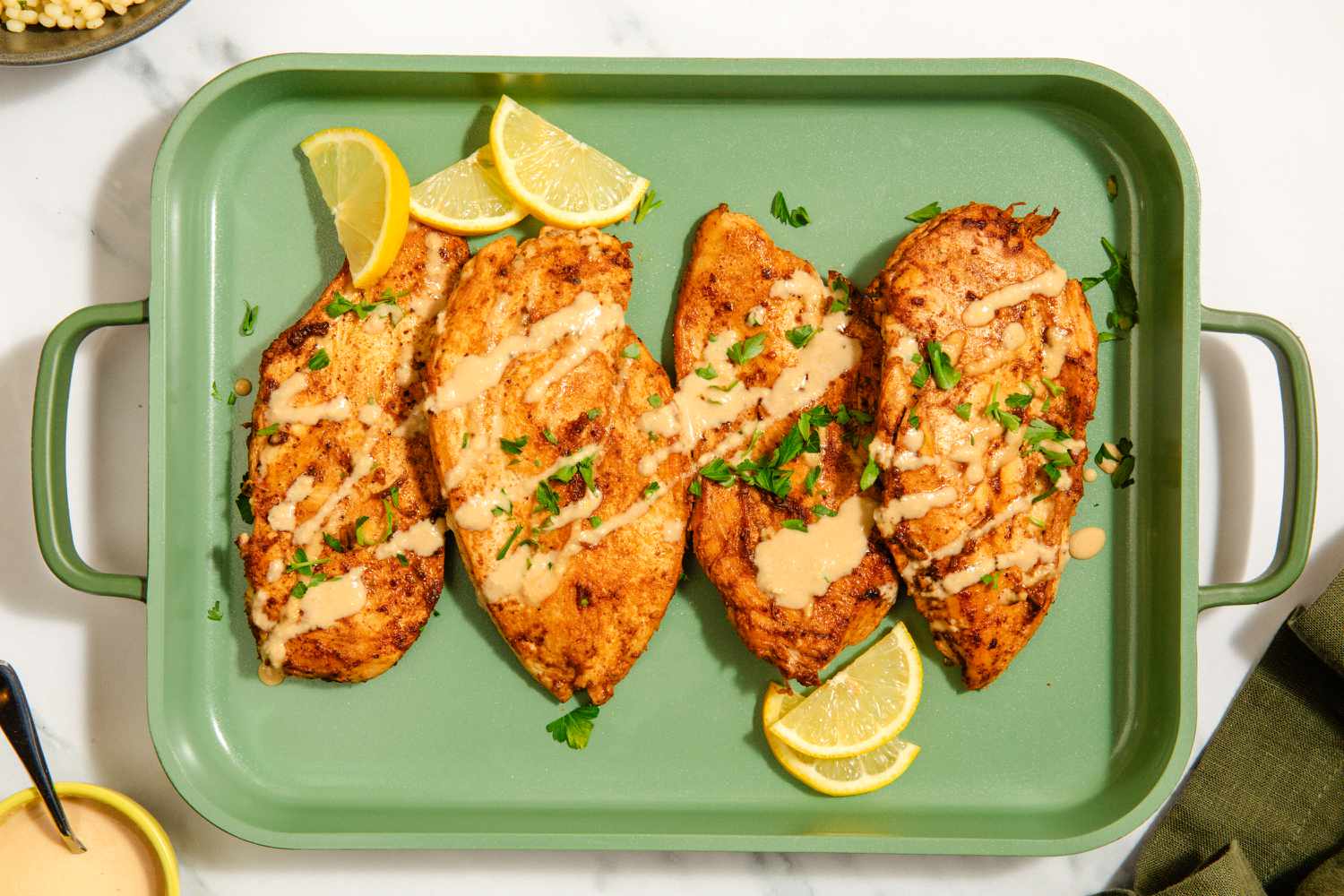 Vue de dessus des escalopes de poulet à l'ail et au tahini sur un plateau vert avec des tranches de citron