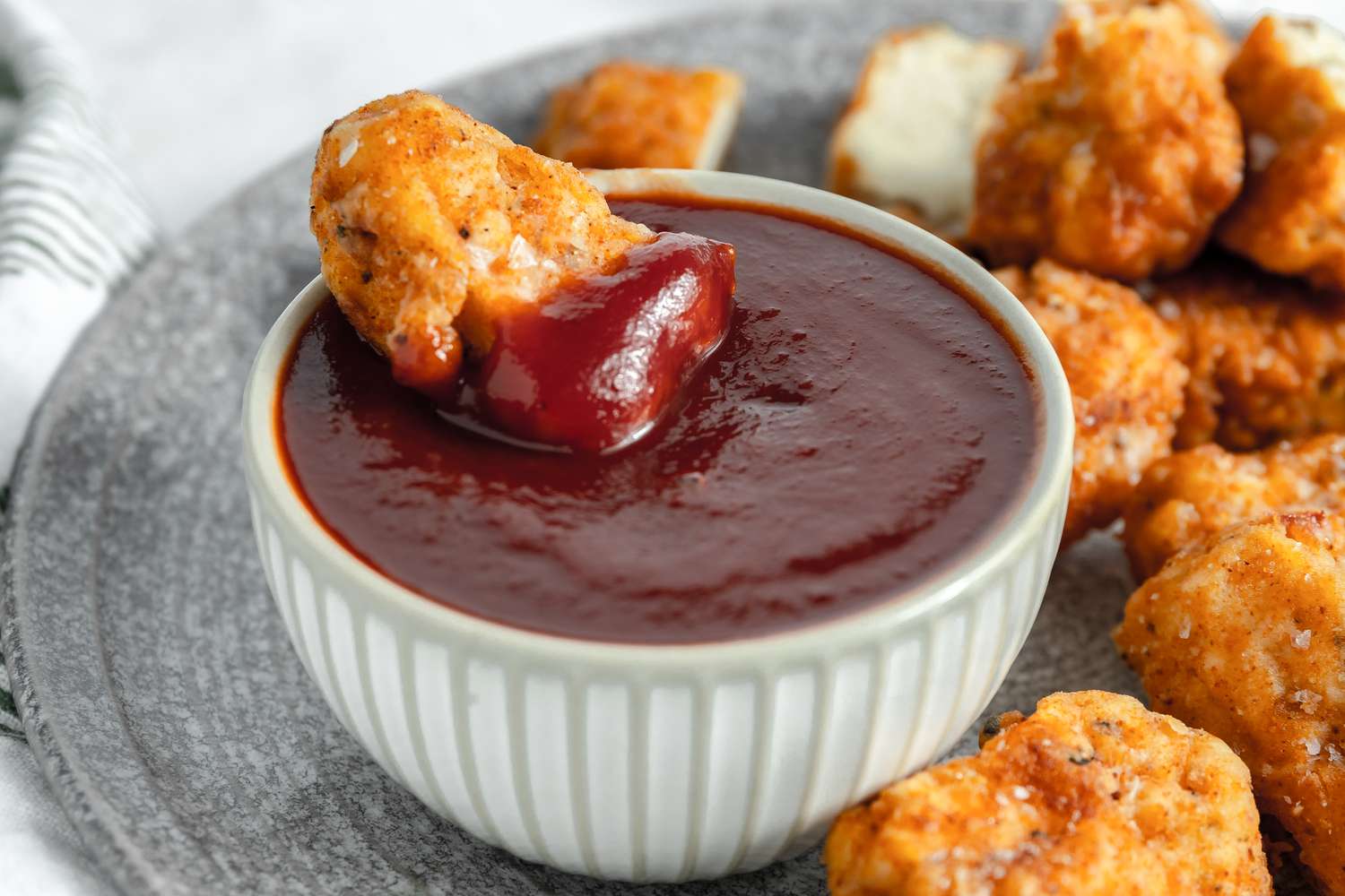 Vegan Chicken Nugget Sitting in a Bowl of Sauce on a Plate with More Vegan Chicken Nuggets