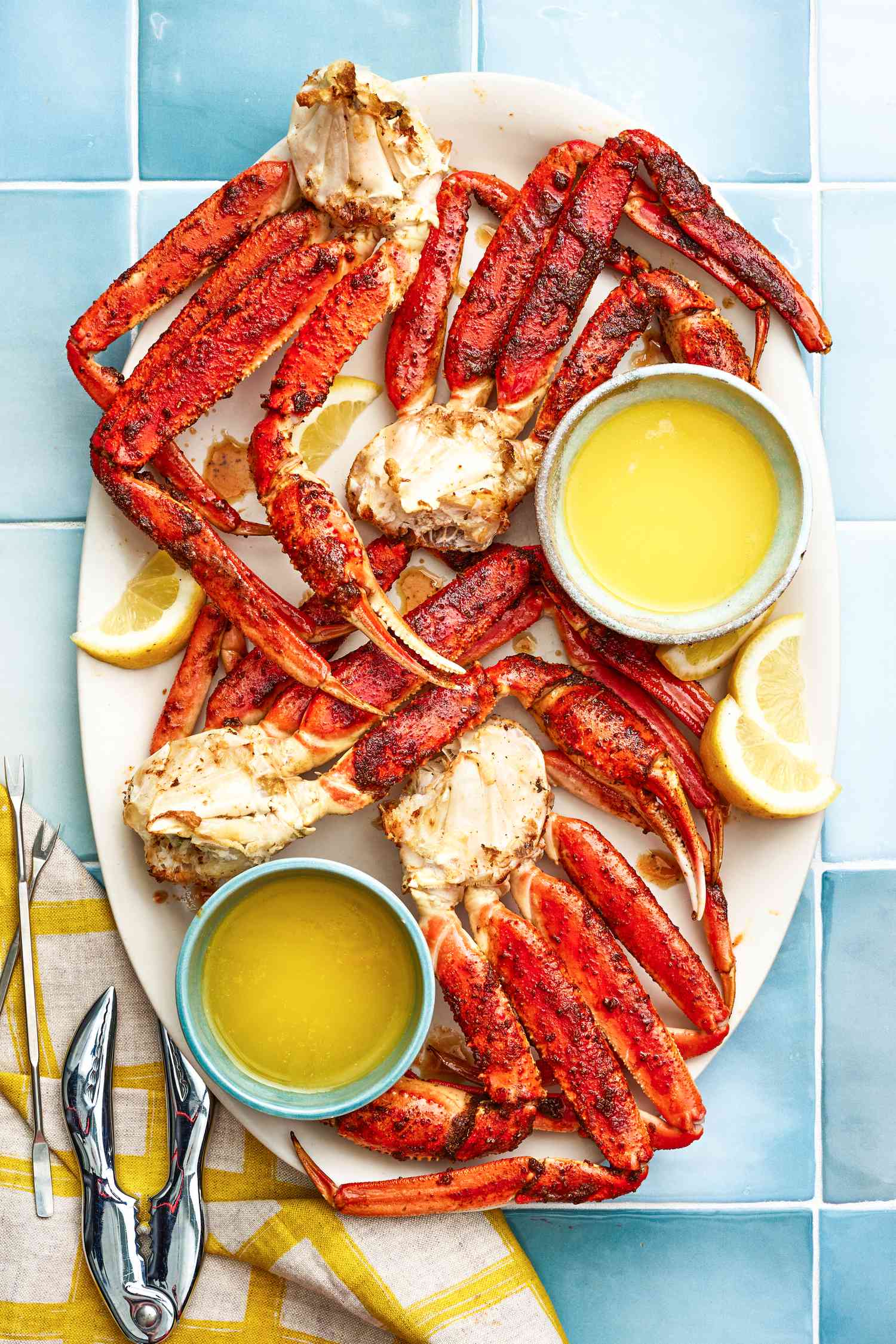 Assiette de pattes de crabe royales cuites au four avec des bols de beurre fondu et des quartiers de citron, à côté des piques à fruits de mer et d’un cracker sur une serviette de table