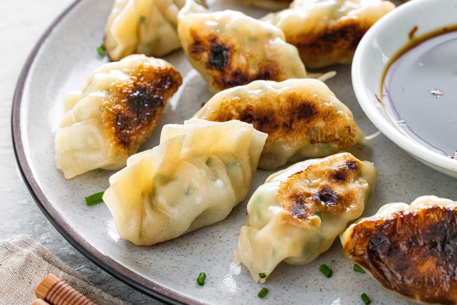 Assiette de dumplings croustillants aux crevettes et à la ciboulette garnie de ciboulette et servie avec une petite soucoupe de sauce soja