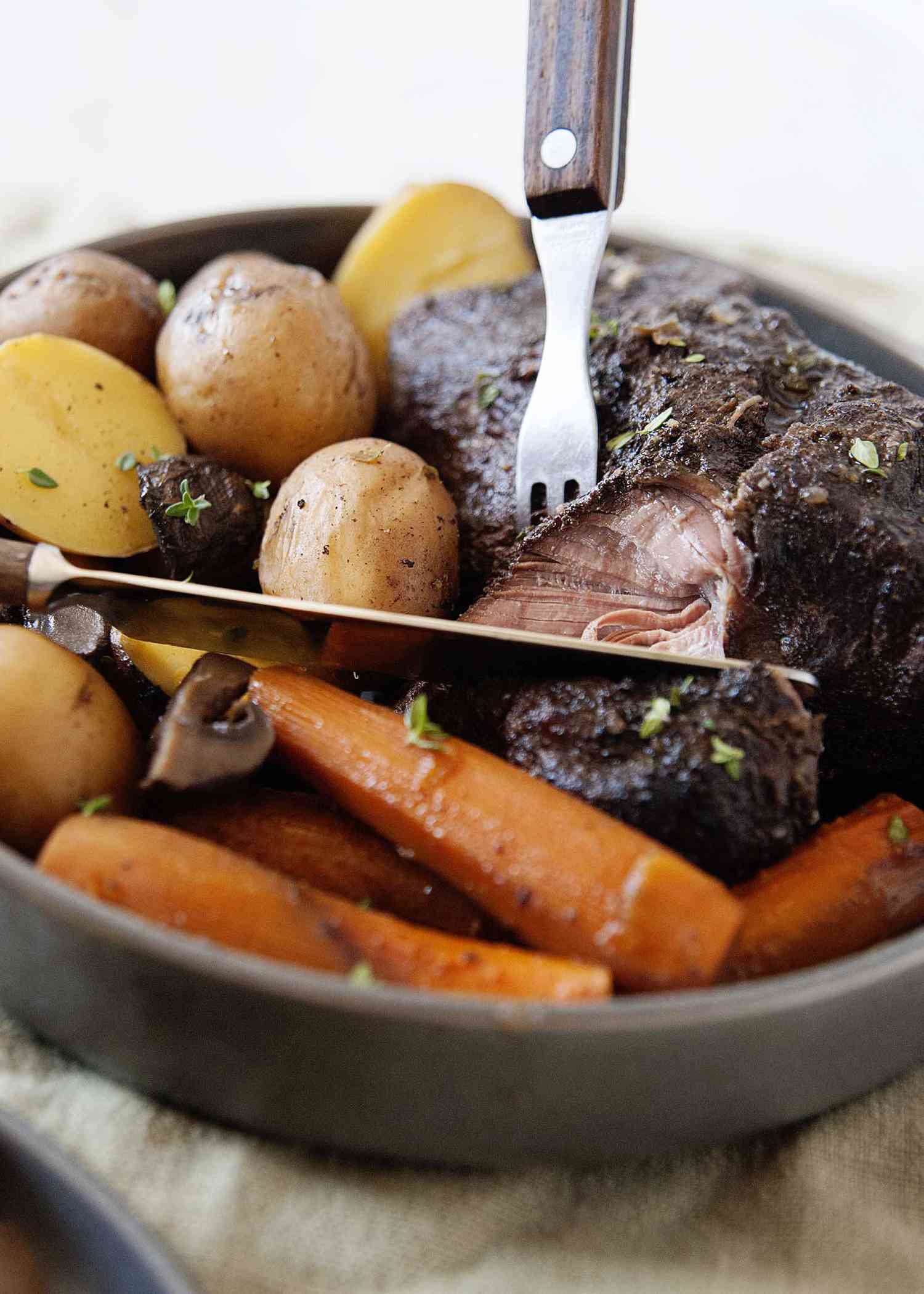 Gros plan sur un rôti tendre cuit dans une mijoteuse avec sauce, carottes et pommes de terre.