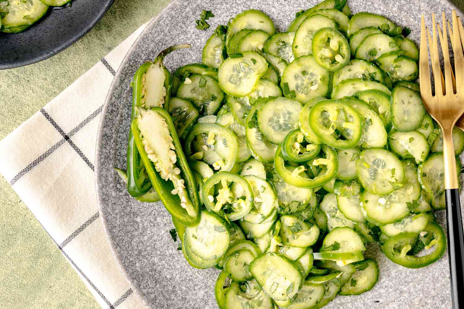 Salade épicée de concombre et de jalapeño sur une assiette avec un jalapeño coupé en deux et des ustensiles