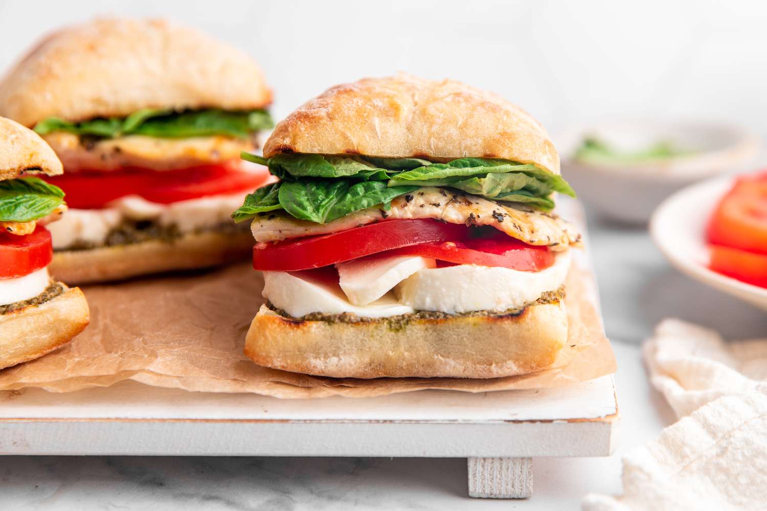 Sandwichs au Poulet Caprese Grillés sur un Plat Doublé de Parchment, et sur le Comptoir à Côté du Plat, Des Assiettes avec des Ingrédients Progresssifs